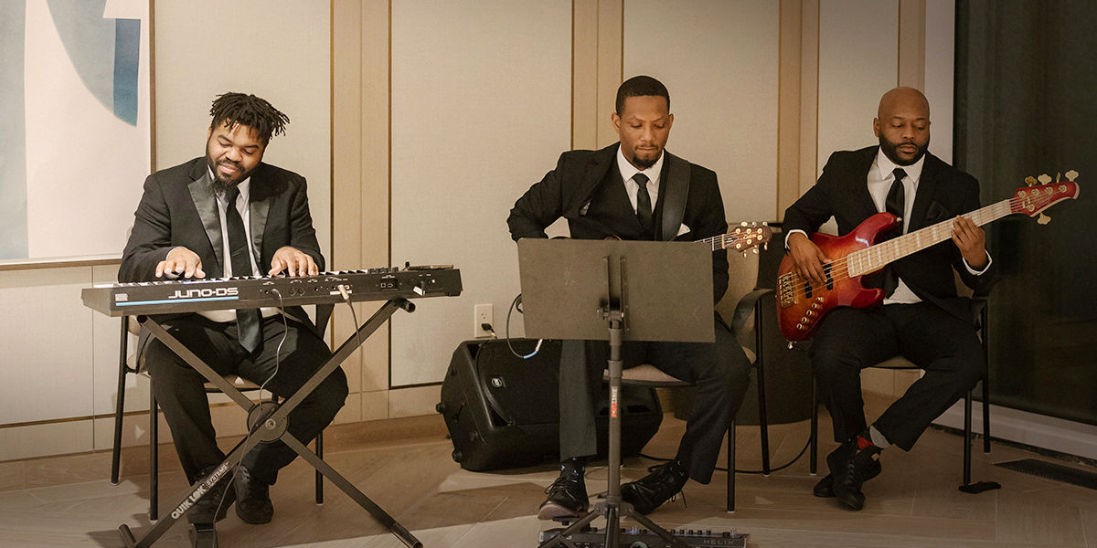 Three male muscicians player keyboard and guitar while wearing suits.