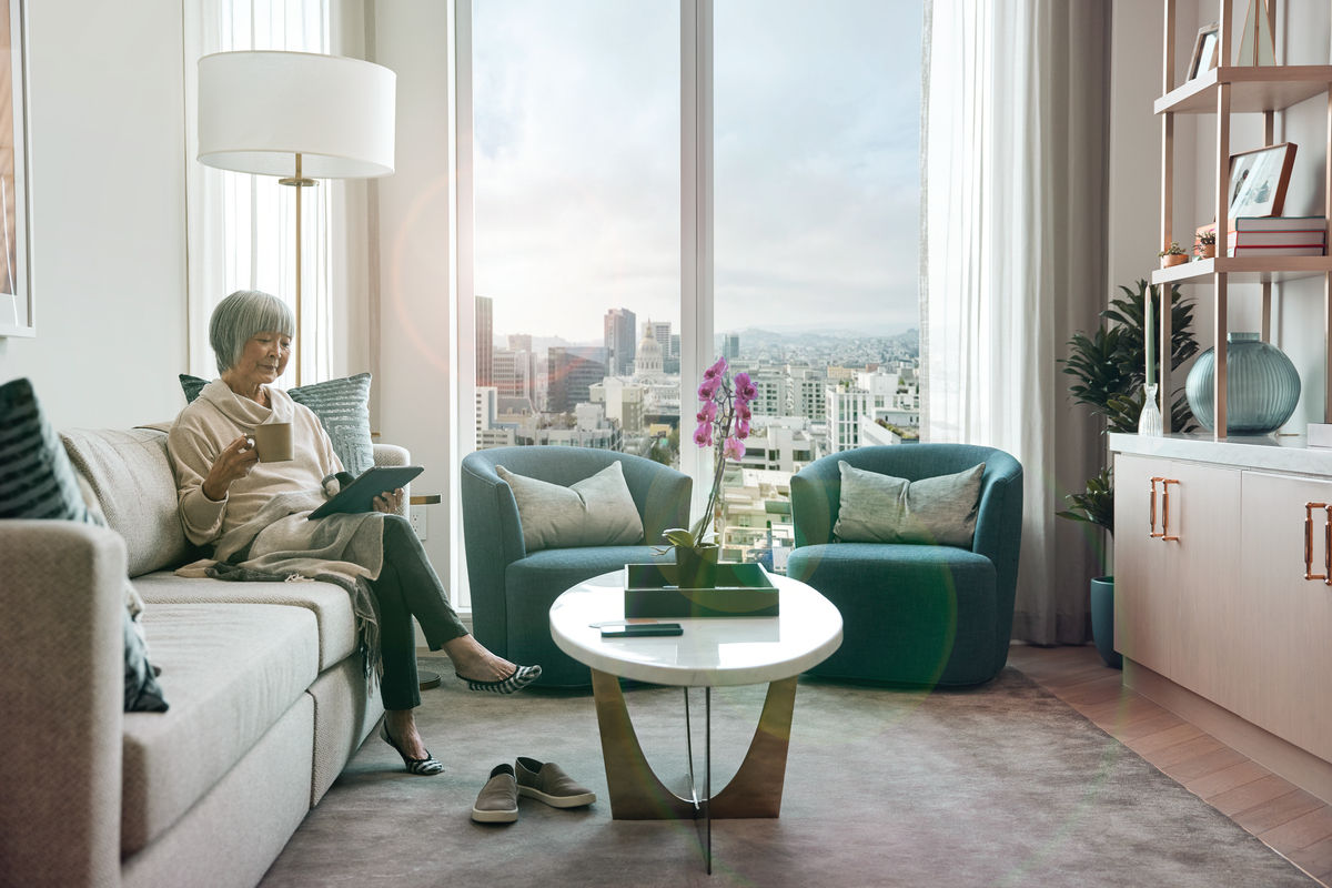 Woman holds a mug while reading her tablet, in a comfortable living room overlooking the city