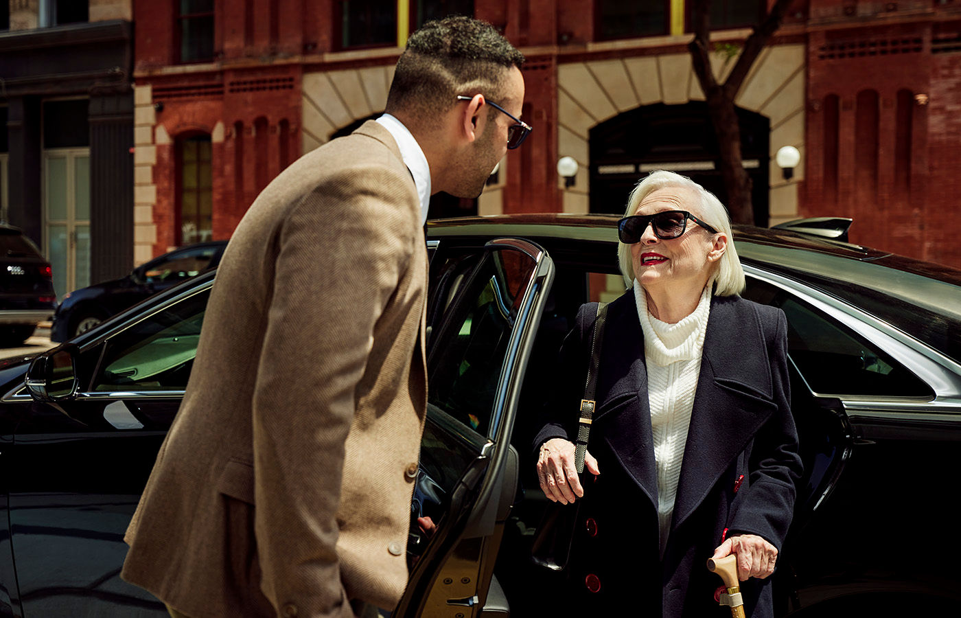 Female senior living resident exiting vehicle and being greeted by friendly Coterie Senior Living employee