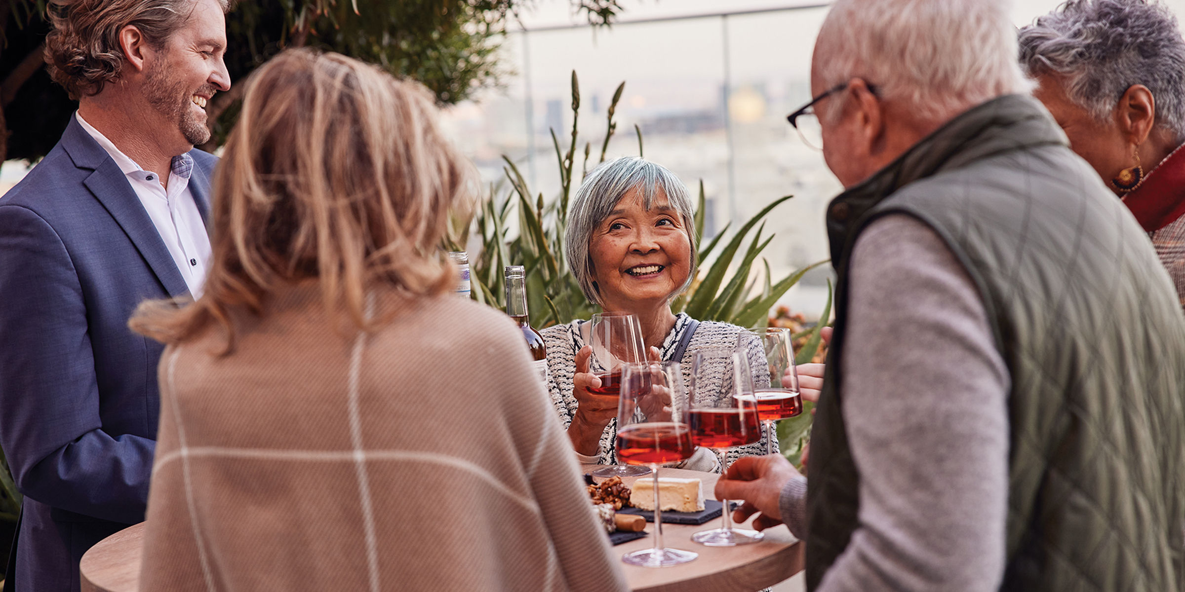Older woman and her family celebrate outside around a table with red wine