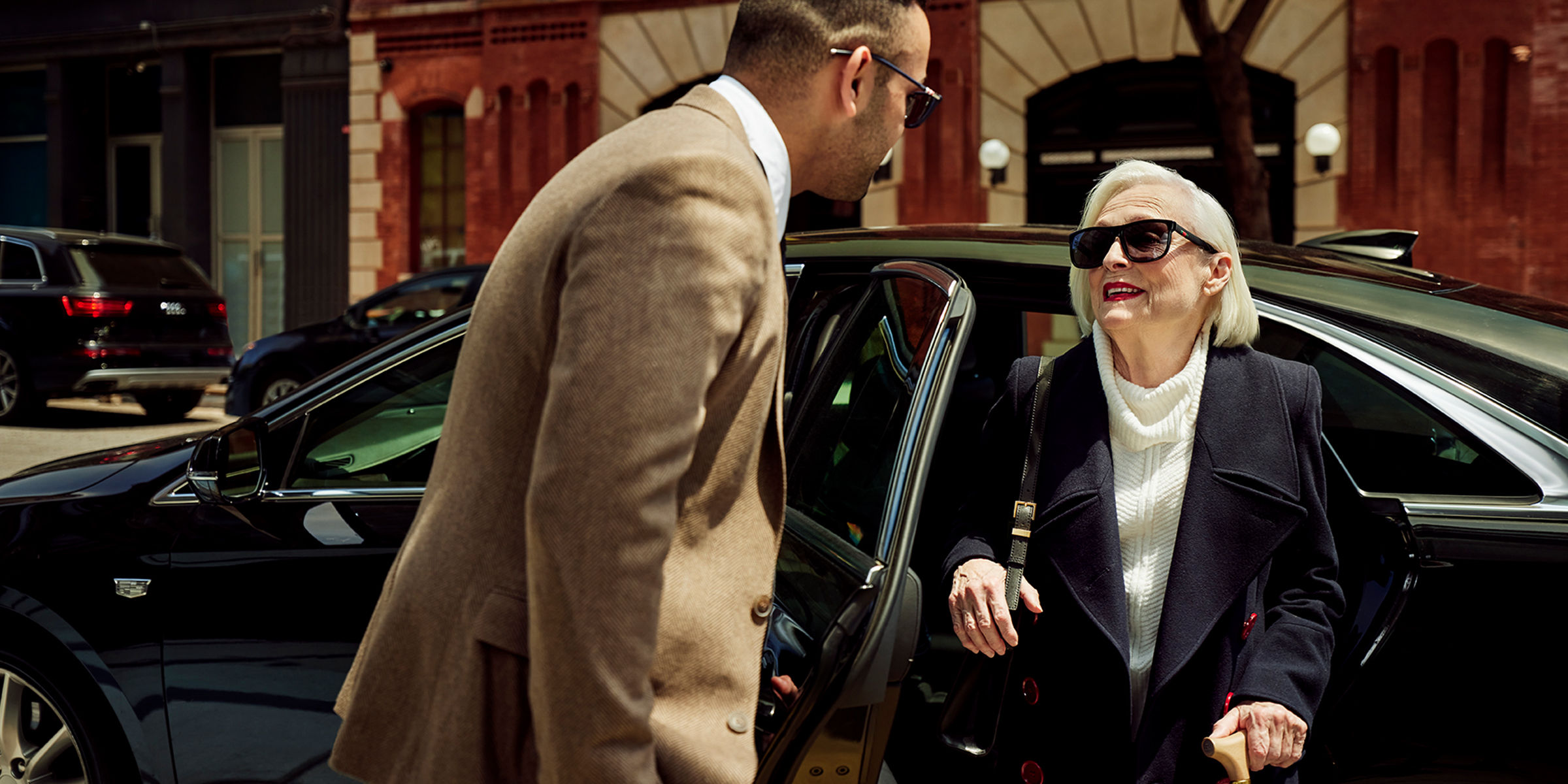 Chauffeur opening a car door for a stylish older woman with a cane