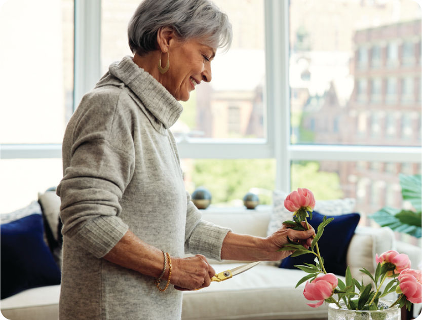 woman trimming flowers in her luxury senior apartment with floor to ceiling windows